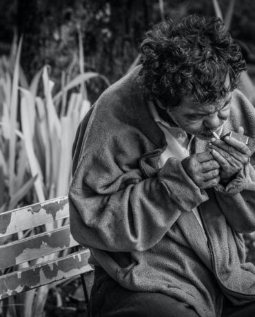 Homeless man smoking cigarette on bench